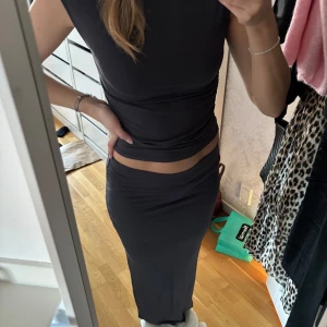 Mörkgrå ärmlös set - Snyggt mörkgrått set med tight passform och ärmlös design. Perfekt för en stilren look. Toppen har en hög hals och både toppen och kjolen är gjord i ett stretchigt material som framhäver figuren. Toppen är i storlek M och kjolen i S