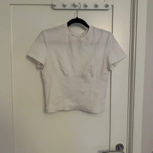 Vit kortärmad topp - Säljer en stilren vit kortärmad topp. Toppen har en figurnära passform och är perfekt för en minimalistisk look. Passar bra till både jeans och kjol.