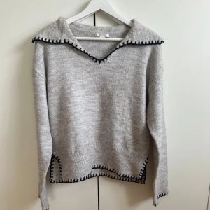 Grå stickad tröja med blå detaljer - Säljer en grå stickad tröja med blå kantdetaljer. Tröjan har en v-ringad krage och långa ärmar. Tröjan är från Gina Young storlek 170 men passar xs-s också💕