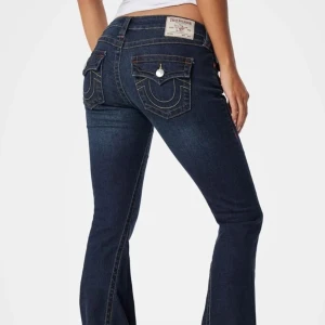 Mörkblå true religion jeans  - Snygga mörkblå jeans från True Religion med bootcut-stil. De har låg midja och dekorativa fickor med knappar bak. En knapp har tyvärr ramlat av på höger ficka… och sedan är det en fläck på höger ben som jag visar på bilden, men inte en jätte tydlig fläck! Utöver det finns det inga defekter. Jag är 1,68 och de är lite korta på mig! ❤️ hör av dig om du vill ha fler bilder! Pris kan diskuteras 🫶🏼