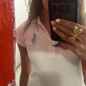 Vit kortklänning från Ralph Lauren - Säljer en stilren vit kortklänning från Ralph Lauren med en klassisk krage och korta ärmar. Klänningen har en broderad blå logotyp på bröstet och en knappslå framtill. Perfekt för en avslappnad och elegant look. Köpt på plick (ej mina bilder utan hennes som sålde den) M i barnstorlek 