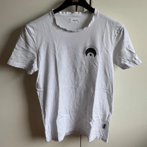 Vit t-shirt med tryck - Säljer en vit t-shirt med ett unikt tryck. Framsidan har en liten grafisk design och baksidan pryds av ett stort öga i svart. Perfekt för en cool och avslappnad stil. Storlek är oklart men rätt så säker på att det är storlek S. Ursäkta att den är lite skrynklig men det beror endast på att den legat i garderoben🙏