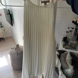 Vit ärmlös blus - Säljer en elegant vit ärmlös blus med plisserad design. Perfekt för sommarens alla tillfällen. Blusen har en luftig passform och en stilren look.