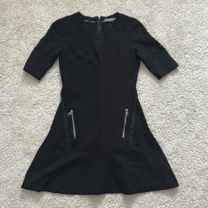 Svart klänning från Calvin Klein Jeans - Snygg svart klänning från Calvin Klein Jeans med trekvartsärmar och dragkedjor framtill. Klänningen har en stilren design med en dragkedja även på baksidan. Perfekt för en chic look!