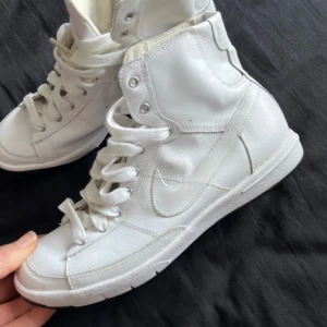 Vita höga sneakers från Nike - Snygga vita höga sneakers från Nike med snörning och rund tå. Skorna har en stilren design med Nike-loggan på sidan och baksidan. Perfekta för en sportig look.