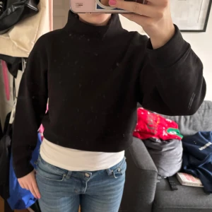 Svart croppad polo tröja från Lindex - Säljer en svart croppad tröja från Lindex. Tröjan har en hög krage och långa ärmar, perfekt för en trendig look. Tillverkad i ett mjukt material och är strl. s