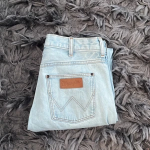 Ljusblå jeans från Wrangler - Snygga ljusblå jeans från Wrangler med klassisk femficksdesign och läderpatch på bakfickan. Perfekta för en avslappnad stil. De har en knappgylf och bälteshällor.