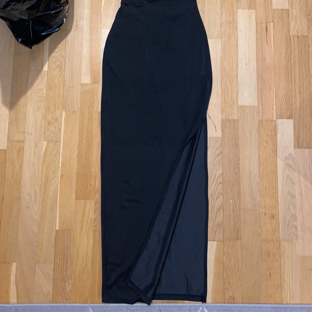 Elegant svart långklänning med smala axelband och snörning i ryggen. Perfekt för en stilren look.. Mekot.