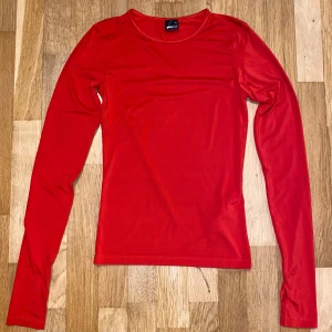 Röd långärmad topp från Gina Tricot - Säljer en stilren röd långärmad topp från Gina Tricot. Perfekt för lager-på-lager eller som den är. Gjord i ett mjukt och stretchigt material för en bekväm passform. Passar till både jeans och kjol. 🌟