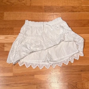 Vit kjol med spetsdetaljer - Charmig vit kjol med vackra spetsdetaljer och elastisk midja. Kjolen har en kort längd och volangkant som ger en extra touch av stil. Aldrig använd. 😇