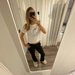 Vit croppad t-shirt med drinkmotiv - Säljer en vit croppad t-shirt med ett stilrent tryck av en drink med citron. T-shirten har korta ärmar och en rund halsringning.