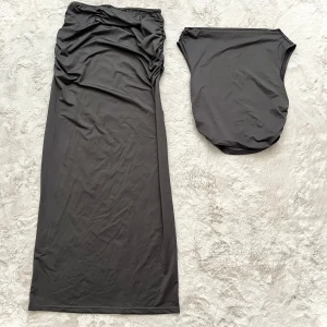 Grå långkjol och topp med rynkdetaljer - Elegant svart långkjol och topp med rynkdetaljer på sidan. Kjolen har en smickrande passform och är perfekt för en stilren look. Tillverkad i ett mjukt och följsamt material.