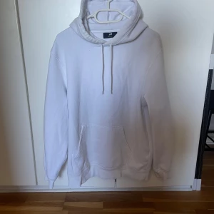 Vit hoodie från H&M - Säljer en stilren vit hoodie från H&M. Den har en klassisk design med en stor ficka framtill och justerbar dragsko i huvan. Perfekt för en avslappnad look.