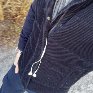 Svart manchester väst - Snygg svart manchester väst med dragkedja och knappar. Perfekt för lager-på-lager stil och passar bra till både vardag och mer uppklädda tillfällen.