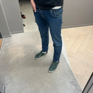 Blå jeans från Jacob Cohen - Snygga blå jeans från Jacob Cohen med knappgylf och klassisk femficksdesign. Perfekta för en stilren look. De har en normal passform och är tillverkade i ett bekvämt denimtyg. Den är av Style 622 och W31 med 98 cm i längd. Näst intill nya och i riktigt bra skick. Alla knappar är intakta och har inga repor på sig. 