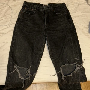 Svarta jeans från Gina - Säljer ett par svarta jeans från Gina med slitna detaljer på knäna. De har en klassisk femficksdesign och knappgylf. Perfekta för en avslappnad stil.
