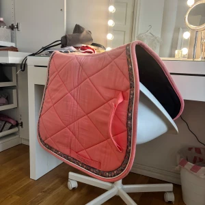 Rosa schabrak från Jacson - Snyggt rosa schabrak från Jacson med quiltat mönster och blommiga detaljer längs kanterna. Perfekt för att ge din ridutrustning en färgglad touch. Bara prövad men tvättas såklart innan d skickas 