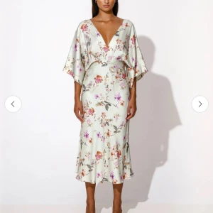 Blommig klänning med öppen rygg - Elegant blommig klänning i ljusgrön nyans med v-ringning och öppen rygg. Klänningen har korta ärmar och ett knytband i midjan för en smickrande passform. Mjukt och luftigt tyg, perfekt för sommarens festligheter! Helt ny med lapparna kvar.