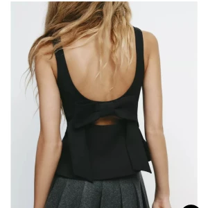 Svart ärmlös topp med rosett - Skit snygg topp med knytning i ryggen. Säljer då den aldrig kommit till användning. Etiketten sitter kvar 