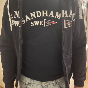 Sandhamn T shirt!  - Säljer en mörkblå t shirt från Sandhamn!  Den har en tryckt text och flaggor på bröstet. Båtig och somrig! (För liten för mig) 