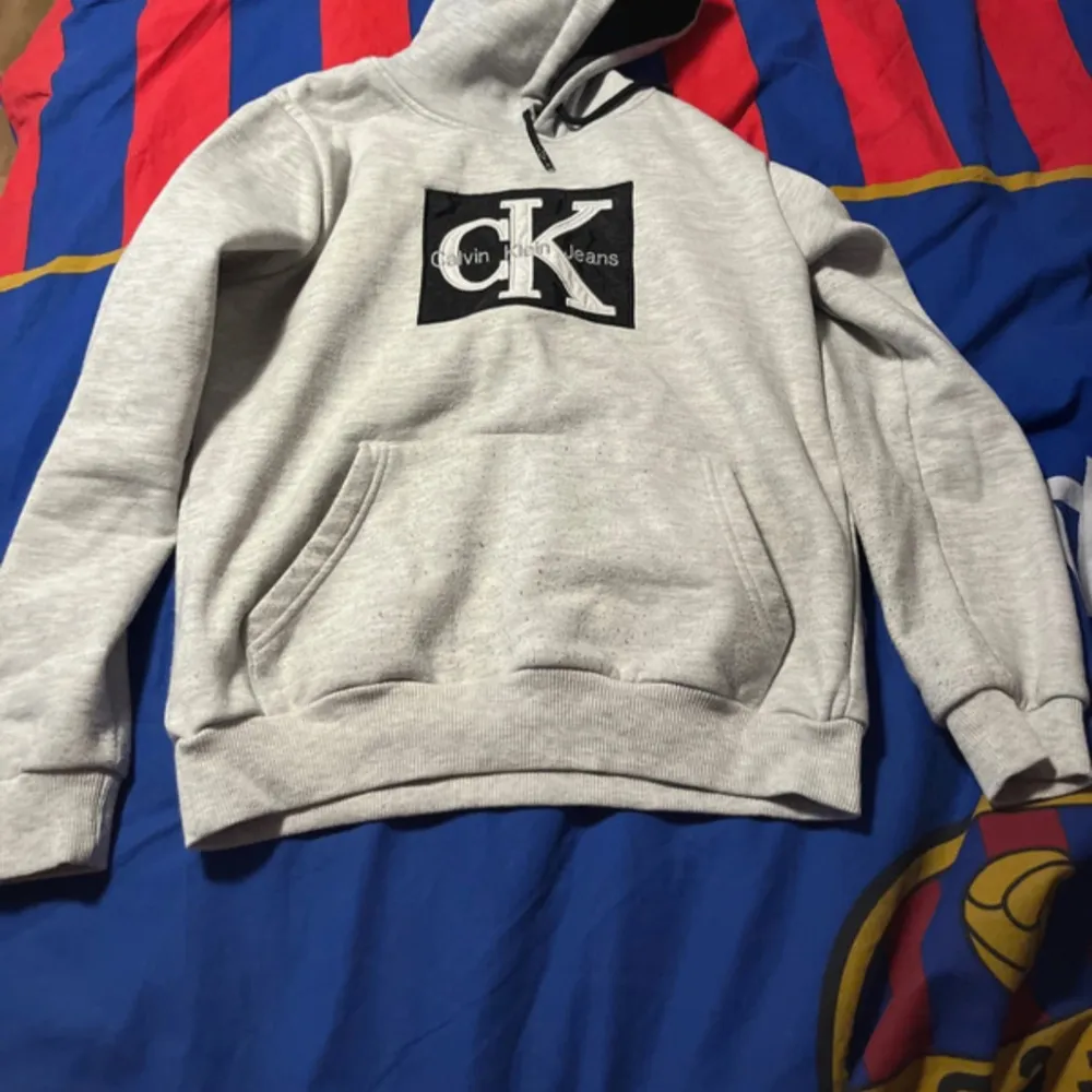 Säljer en stilren grå hoodie från Calvin Klein med deras ikoniska logga på bröstet. Tröjan har en klassisk känguruficka och en bekväm huva med dragsko. Perfekt för en avslappnad look. Använd 1-2 gånger. Säljer pga inte gillar den.. Neuletakit & Villapaidat.