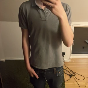 Grå pikétröja - Säljer en stilren grå pikétröja med krage och knappar. Perfekt för en avslappnad men ändå snygg look. Passar bra till jeans eller chinos.