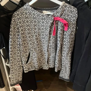 Mönstrad tröja från Odd Molly - Säljer en snygg mönstrad tröja från Odd Molly i svart och vit med en rosa knytning på framsidan. Tröjan har långa ärmar och ett unikt mönster. 