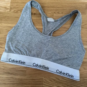 Grå sporttopp från Calvin Klein - Säljer en grå sporttopp från Calvin Klein med ett brett elastiskt band med logotypen. Toppen är ärmlös och har en bekväm passform, perfekt för träning eller vardagsbruk.