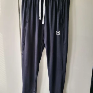 Under armour byxor - Säljer ett par svarta träningsbyxor från Under Armour med vit dragsko i midjan och logotyp på benet. Byxorna har en loose passform och är perfekta för träning. Tillverkade i Jordanien.