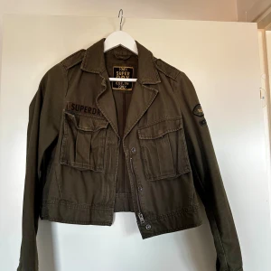 Jacka från Superdry - En snygg, militärgrön jacka från Superdry. Perfekt till våren! Knappen på ena fickan har lossnat, men har sytt dit nya knappar så fickan fungerar utan problem och syns ingenting. Mer bilder kan fås vid begäran 💚☺️