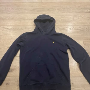 Mörkblå hoodie med logotyp - Säljer en mörkblå hoodie med en liten gul logotyp på bröstet. Tröjan har en klassisk känguruficka och en bekväm huva. Perfekt för en avslappnad stil.