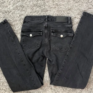 Svarta lågmidjade bootcut jeans  - Svarta jeansbyxor från 157 med klassisk femficksdesign och raka ben. Byxorna har silverfärgade knappar och detaljerade bakfickor med lock och knapp. Använda fåtal gånger och därför säljer jag dom då de inte kommer till användning. De har ett litet riv märke på högra låret men det är inget men tänker på💞