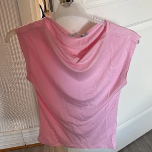 Ljusrosa ärmlös topp med draperad hals - Säljer en ljusrosa ärmlös topp med snygg draperad halsringning. Perfekt för dig som gillar en enkel men stilren look. Mjuk och skön i materialet, passar bra till både jeans och kjol. Storlek s. 50kr. Har även i blå