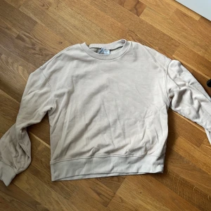 Beige sweatshirt från hm - Säljer en enkel och stilren beige sweatshirt från Divided. Tröjan har rund halsringning och långa ärmar, perfekt för en avslappnad look. Mjuk bomullskänsla och ribbade muddar vid ärmslut och nederkant.