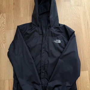 Svart vindjacka från The North Face - Säljer en välbevarad "The North Face" vindjacka. Den är perfekt för utomhusaktiviteter, lätt och andas, samtidigt som den ger utmärkt skydd mot vind och lätt regn. Jackan är i utmärkt skick, inga skador och tveka inte att fråga vid funderingar! 🐻‍❄️