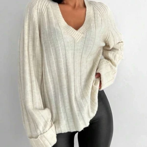 Beige ribbad stickad tröja med v-ringning - Säljer en oversized beige stickad tröja med v-ringning och ribbat mönster. Tröjan har långa ärmar och en avslappnad passform. 