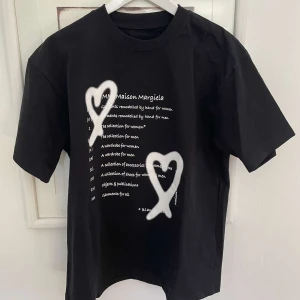 Svart t-shirt från Maison Margiela med tryck - Svart t-shirt från Maison Margiela med vitt tryck och två stora hjärtan framtill. Perfekt för dig som gillar streetwear och unika designer.