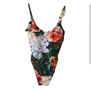 Blommig baddräkt från Andres Sarda - Snygg baddräkt med blommigt mönster i grönt, rött, blått och beige från Andres Sarda. Axelbanden har en unik detalj med pärlliknande dekoration. Perfekt för strand eller pool!