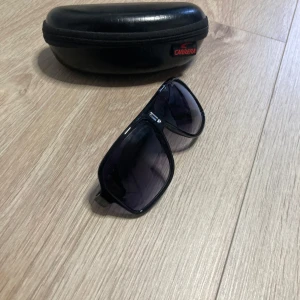 Svarta solglasögon från Carrera - Snygga svarta solglasögon från Carrera med klassisk pilotform och mörka glas. Bågarna och perfekta för att ge din stil en cool touch. Utan fodral 