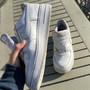Vita Nike Air Force 1 sneakers - Säljer ett par klassiska vita Nike Air Force 1 sneakers. Skorna har en låg modell med rund tå, platt sula och tydlig Nike-logga på sidan. Tillverkade i skinn och kommer med vita skosnören. Perfekta för en stilren och sportig look.
