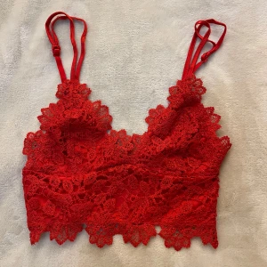 Röd spets bralette - Snygg röd bralette med spetsdetaljer och dubbla axelband. Toppen har vackert blommönster i spetsen och justerbara axelband för bästa passform. Perfekt för att ge outfiten en extra touch av färg och stil.