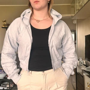 Ljusblå croppad hoodie - Säljer en ljusblå croppad hoodie med dragkedja och huva. Jackan har långa ärmar och ribbade muddar. Perfekt för en avslappnad stil.