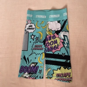 Förglada träningsshorts från Stronger - Coola träningsshorts från Stronger med pop art-inspirerat tryck i turkos, svart, rosa och gul. Hög midja med bred resår och texten STRONGER. Tillverkade i återvunnen polyester och elastan för stretchig passform. Tvättar innan jag skickar produkten😊