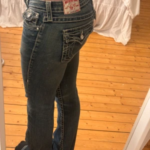 Mörkblå jeansbyxor från True Religion - Säljer ett par mörkblå jeansbyxor från True Religion, fatstitch och diamant detaljer, låg midja . De fick hål bak som jag sytt igen, skriv för bilder på det🥰