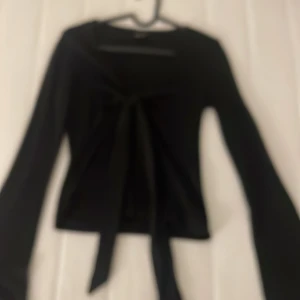 Svart knytblus från Gina Tricot - Säljer en svart långärmad topp från Gina Tricot med knyt framtill. Perfekt att styla till olika outfits och passar dig som gillar en enkel men trendig look.
