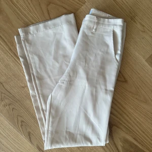 Beiga kostymbyxor från Madlady - Snygga beiga kostymbyxor från Madlady med klassisk passform och hällor för bälte. Byxorna har raka ben och sidofickor, perfekta för en stilren look.