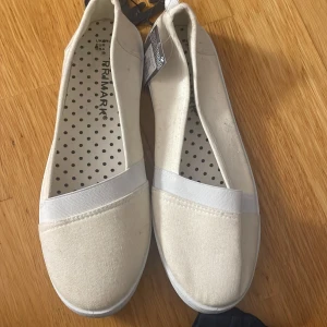 Vita ballerinaskor  - Säljer ett par vita ballerinaskor från Primark med elastiskt band över foten. Skorna har rund tå, platt sula och är tillverkade i textilmaterial. Perfekta för en enkel och stilren look. Aldriga använda 