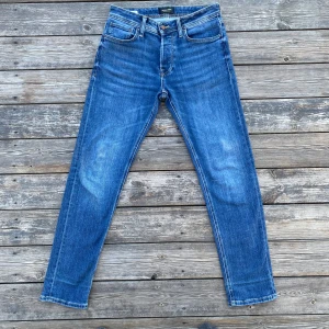 Blå jeans från Jack & Jones - Säljer ett par klassiska blå jeans från Jack & Jones med fem fickor och gylf med dragkedja. Jeansen har raka ben och normal passform, perfekt för en avslappnad stil. Tidlös design med snygga kontrastsömmar och läderpatch bak i midjan.
