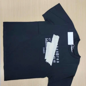 Svart t-shirt med vit text - Säljer en svart t-shirt från Maison Margiela med vit text och siffror tryckta på bröstet. Klassisk rund hals och korta ärmar. Perfekt för dig som gillar stilrena och trendiga plagg.