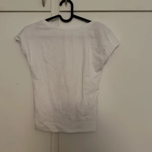 Vit topp med öppen rygg - Säljer en vit topp med korta ärmar och öppen rygg. Perfekt för sommaren och enkel att matcha med olika outfits. Tunn och mjuk i materialet.